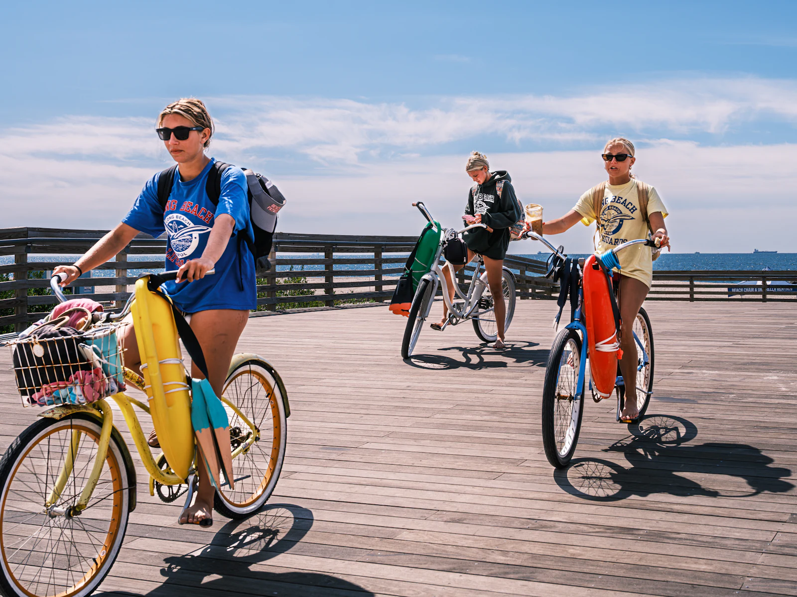 People riding beach-cruiser bikes along a boardwalk by the ocean in Pacific Beach