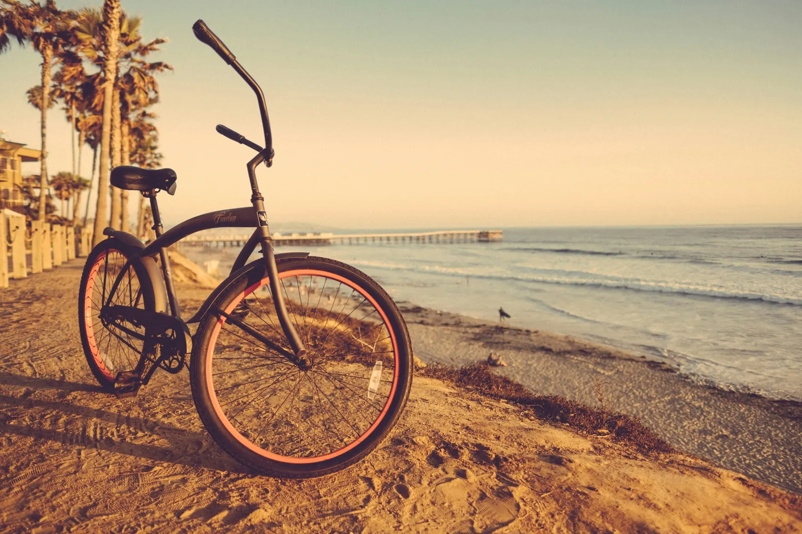 Beach cruiser bicycle parked on the sand at golden hour with a pier behind
